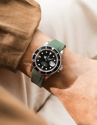 Green FKM rubber strap integrated for original clasp on Rolex Submariner 16610LN full steel, black ceramic bezel, black dial, angled top-down wrist shot, smooth olive green strap texture, brown linen jacket sleeve, cream background