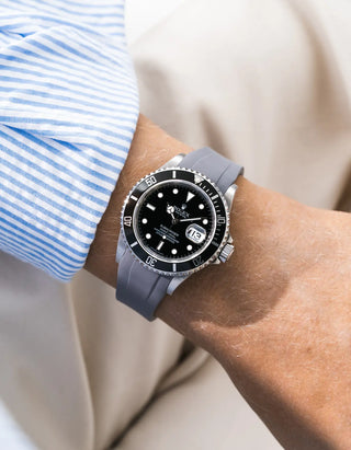 Grey FKM rubber strap integrated for original clasp on Rolex Submariner 16610LN full steel, black ceramic bezel, black dial, straight front-facing wrist shot, smooth strap texture, beige background, blue striped shirt cuff partially visible