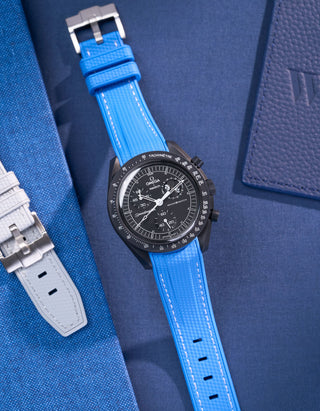 MoonSwatch Mission to Moonphase new Moon with vertech neptune blue rubber strap placed on blue fabric surface next to blue pouch