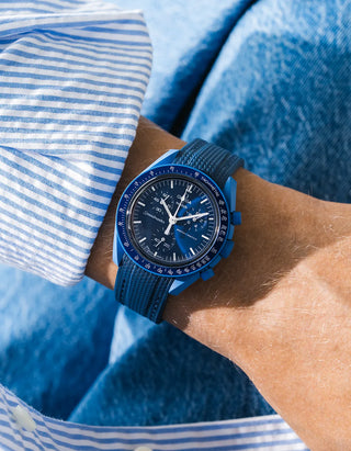 Navy blue rubber strap fitted to an OMEGA x Swatch MoonSwatch Mission to Neptune watch, worn on the wrist in a lifestyle shot with clothing visible