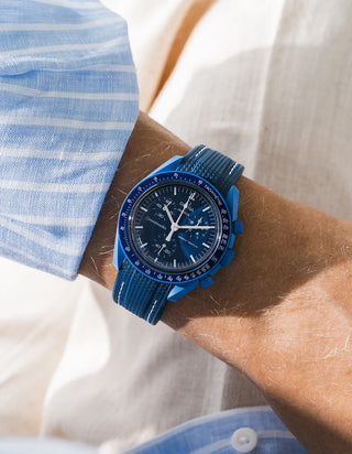 Navy blue rubber strap with white stitching fitted to an OMEGA x Swatch MoonSwatch Mission to Neptune watch, worn on the wrist in a lifestyle shot with clothing visible