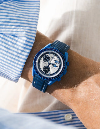 Navy blue rubber strap with white stitching fitted to an OMEGA x Swatch MoonSwatch Mission to the Super Blue Moonphase watch, worn on the wrist in a lifestyle shot with clothing visible