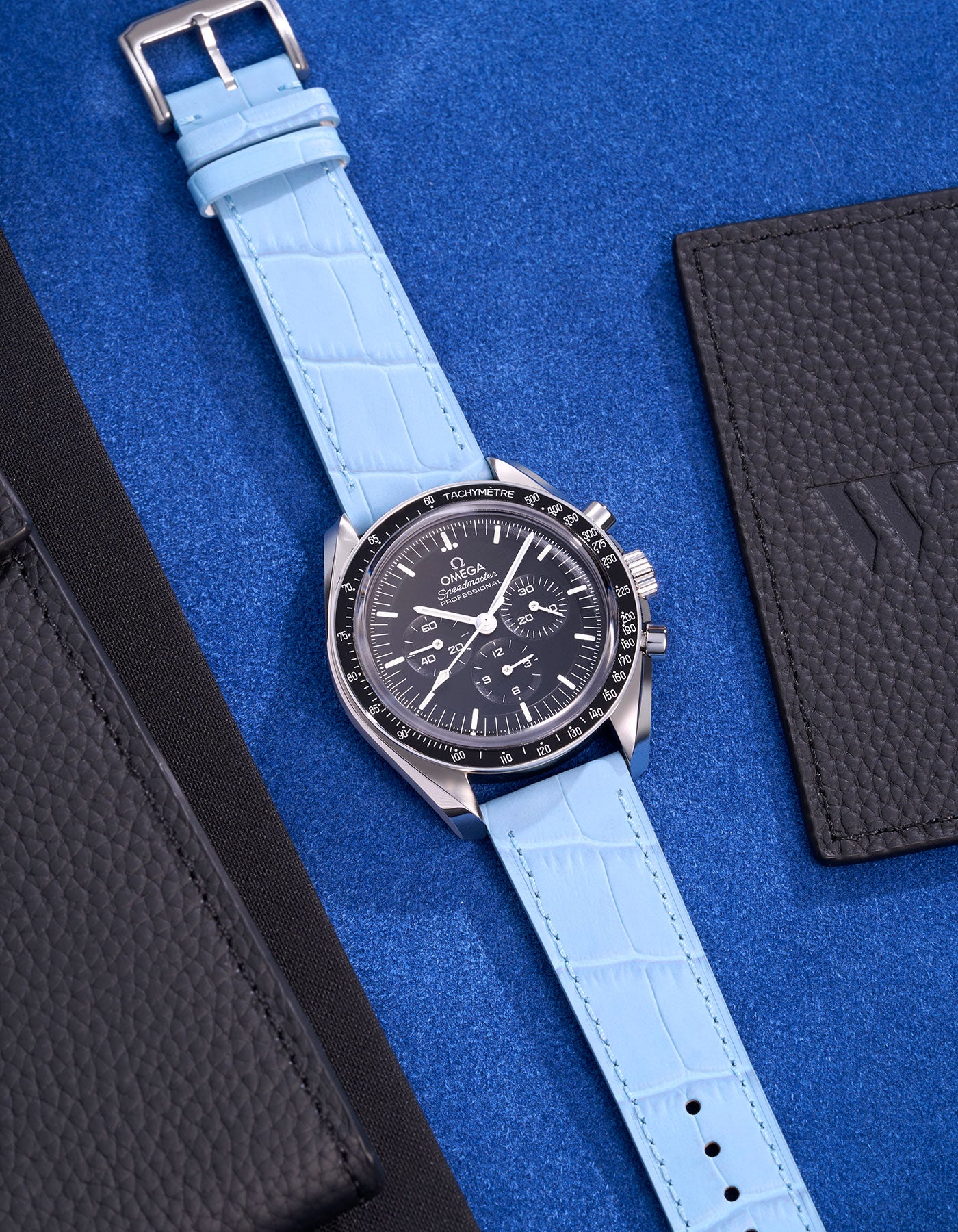 Omega Speedmaster watch with a light blue alligator leather strap on a blue background