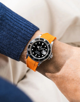 Orange Vertech FKM rubber strap integrated for original clasp on Rolex Submariner 16610LN full steel, black ceramic bezel, black dial, angled top-down wrist shot, Vertech crosshatch texture clearly visible on strap, navy blue knit sweater sleeve, beige background