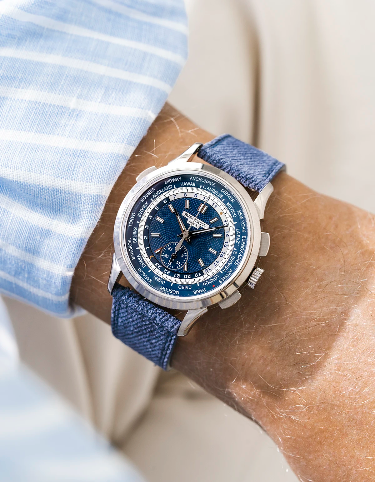Patek Worldtimer on a blue denim leather watch strap from Wristbuddys on a persons wrist wearing a blue striped shirt