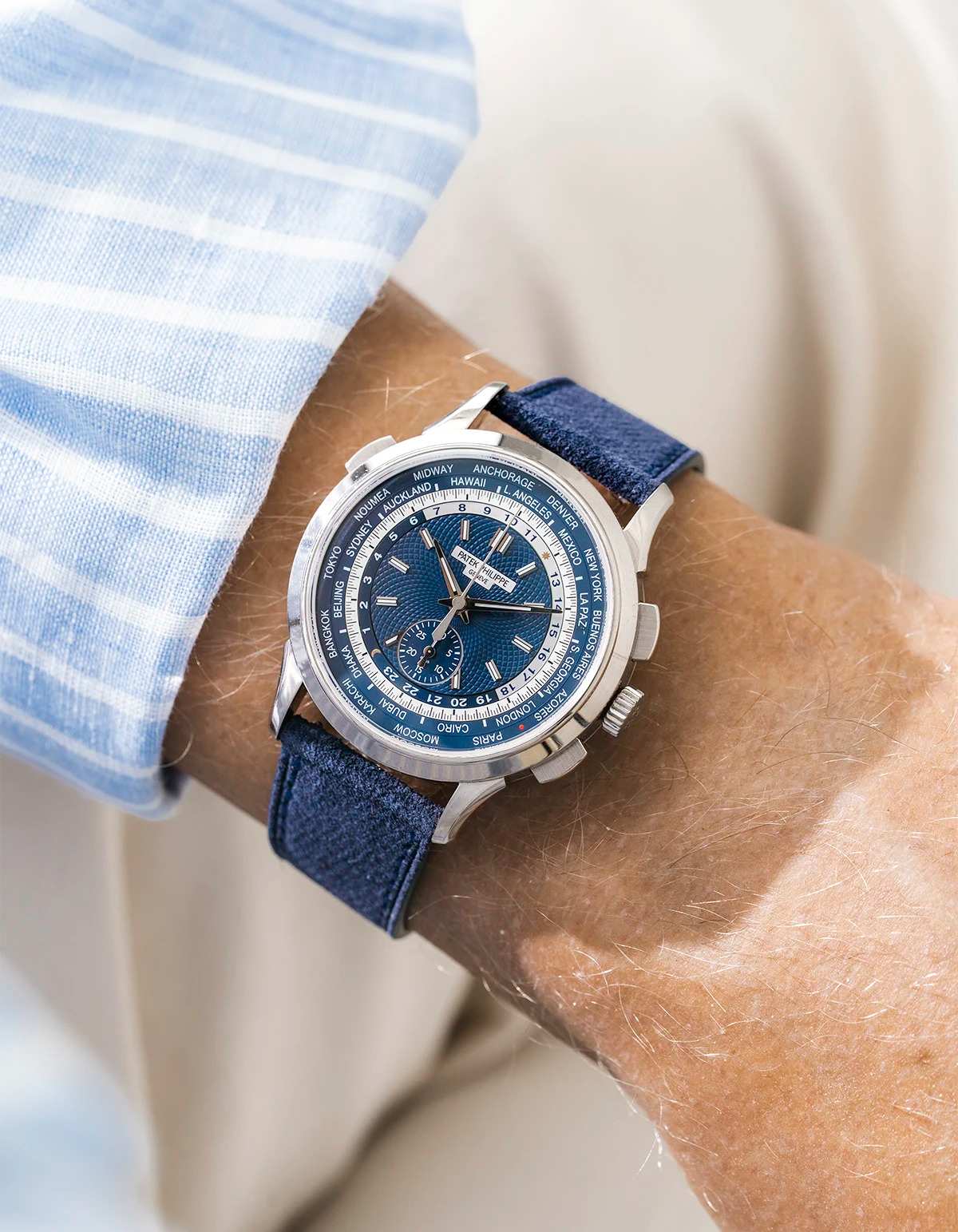 Patek Worldtimer on a navy blue denim leather watch strap from Wristbuddys on a persons wrist wearing a blue striped shirt