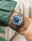 Patek Worldtimer with a blue face and grey epsom leather watch strap from Wristbuddys on a wrist, wearing a green shirt.