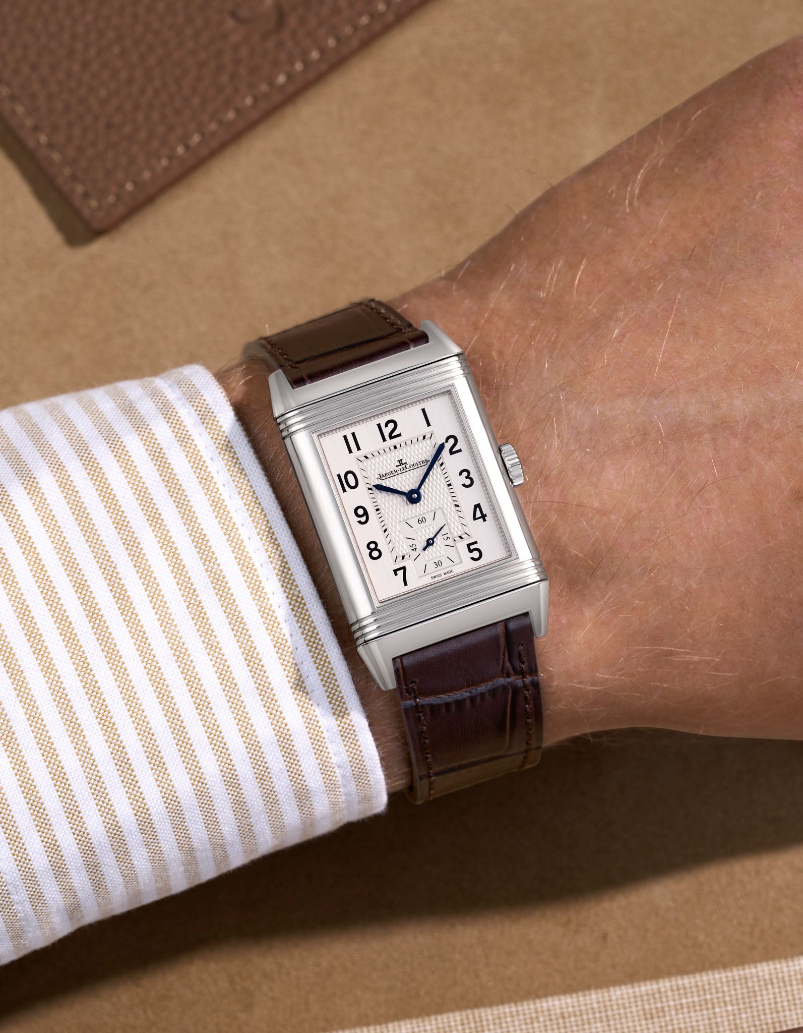 JLC Reverso steel watch with a dark brown embossed alligator leather watch strap on a beige background