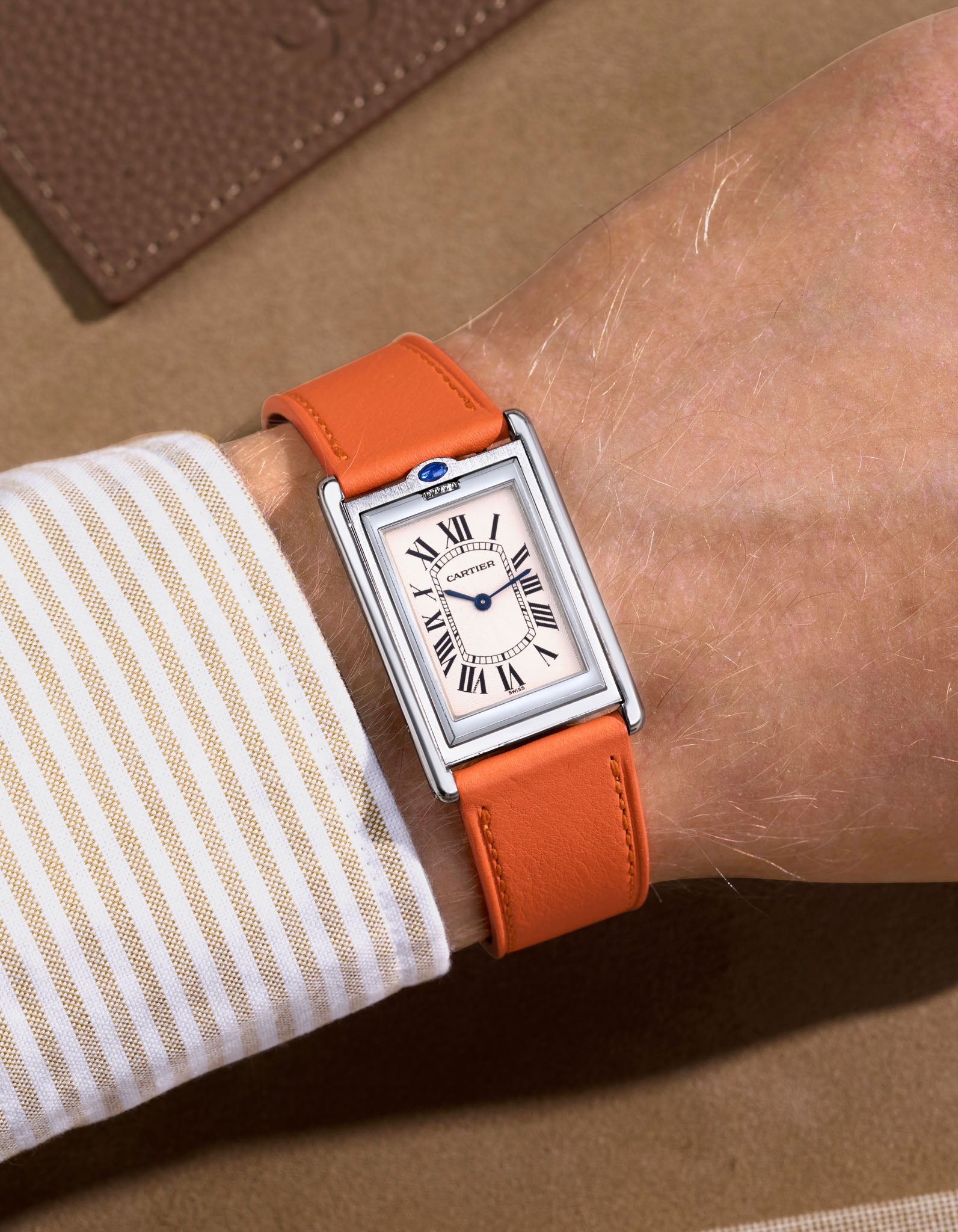 cartier basculante with white dial and with a orange cowhide leather watch strap on a beige background