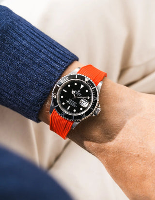 Red Vertech FKM rubber strap integrated for original clasp on Rolex Submariner 16610LN full steel, black ceramic bezel, black dial, straight front-facing wrist shot, Vertech crosshatch texture clearly visible on red-orange strap, navy blue knit sweater sleeve, cream background