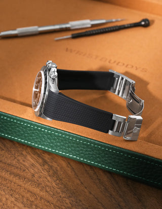 Black textured FKM rubber watch band for Rolex Daytona 16520, seamless case integration with original clasp, resting on a leather valet tray.