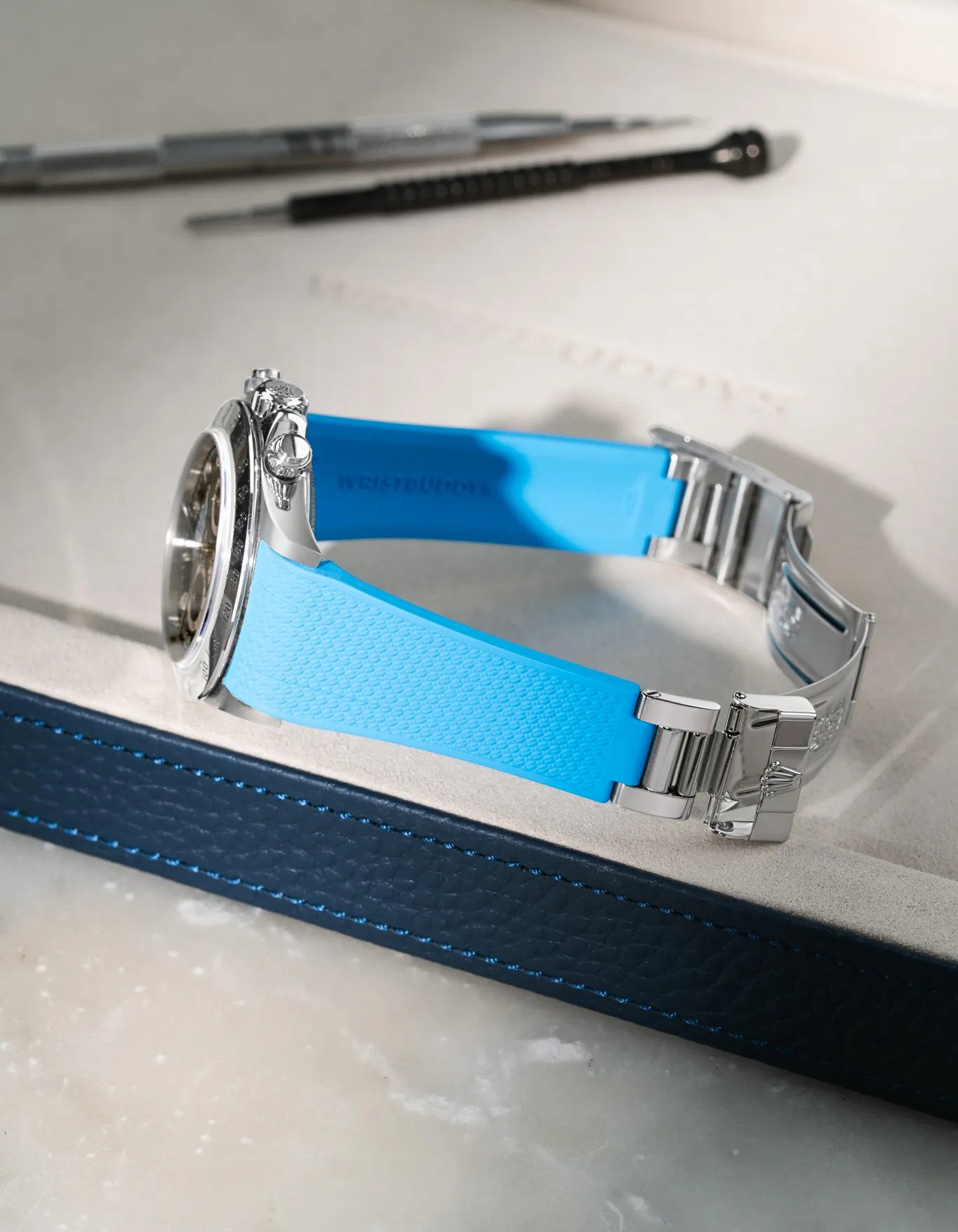 Capri Blue Vertech FKM rubber watch band for Rolex Daytona 16520, custom integrated fit with original clasp, resting on a brown leather valet tray.