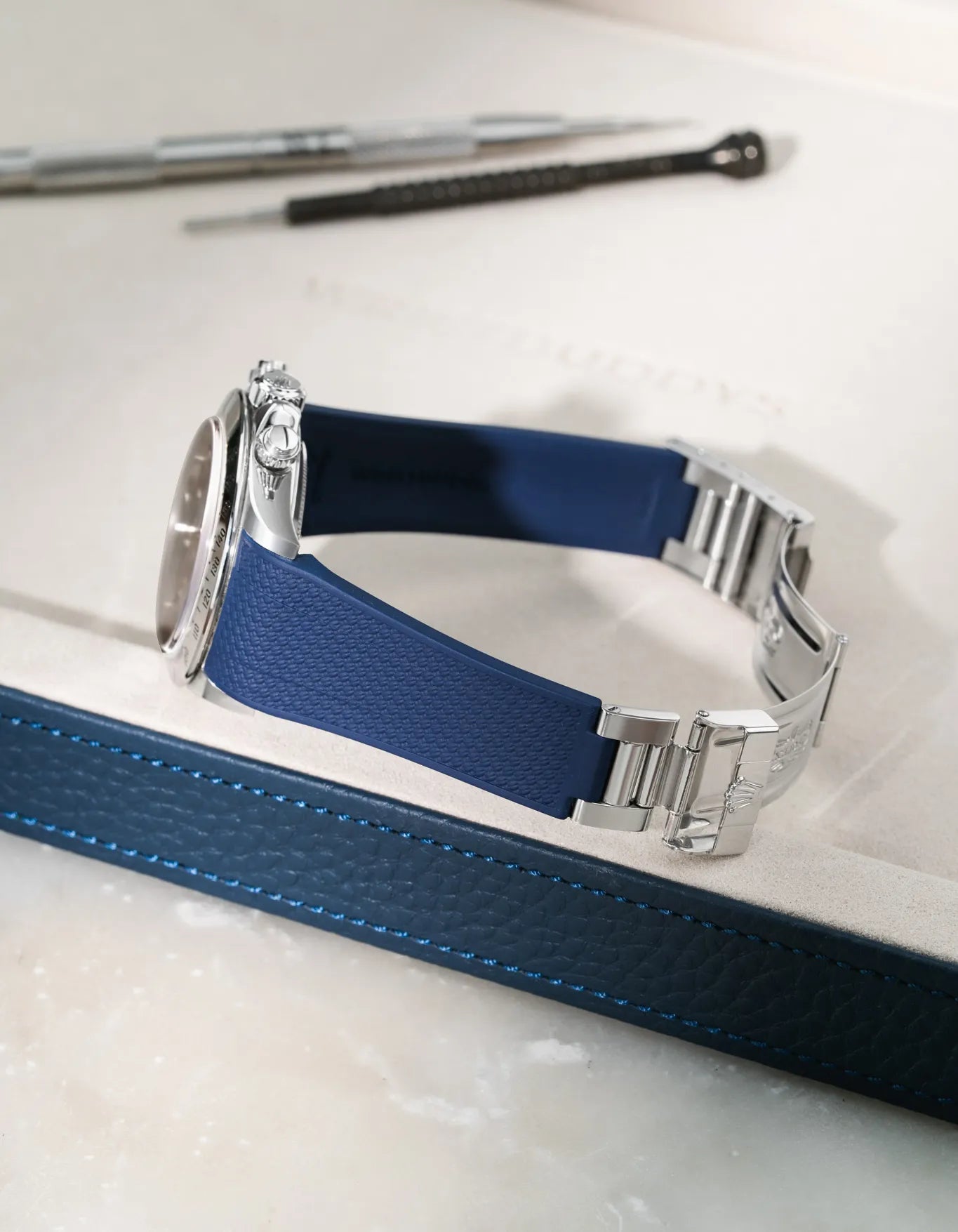Navy Blue integrated FKM rubber strap for Rolex Daytona 16520, textured finish and original clasp, resting on a leather valet tray.
