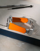 Bright Orange textured integrated FKM rubber strap for Rolex Daytona 16520, fits original clasp, resting on a leather valet tray.