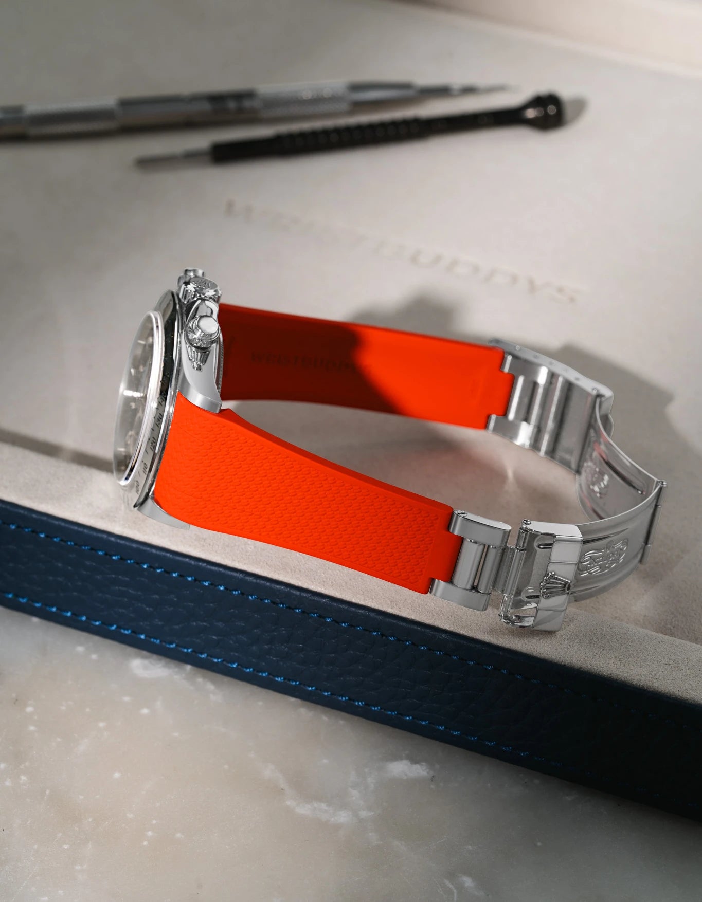 Red integrated FKM rubber watch strap for Rolex Daytona 16520 with texture, using original clasp, resting on a brown leather valet tray.