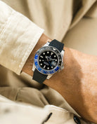 Close-up of a person wearing a Rolex GMT Master 2 Batman model watch with a beige jacket sleeve and a black FKM rubber watch strap from Wristbuddys