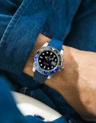 Close-up of a person wearing a Rolex GMT Master 2 Batman model watch with a blue jacket sleeve and a blue FKM rubber watch strap from Wristbuddys