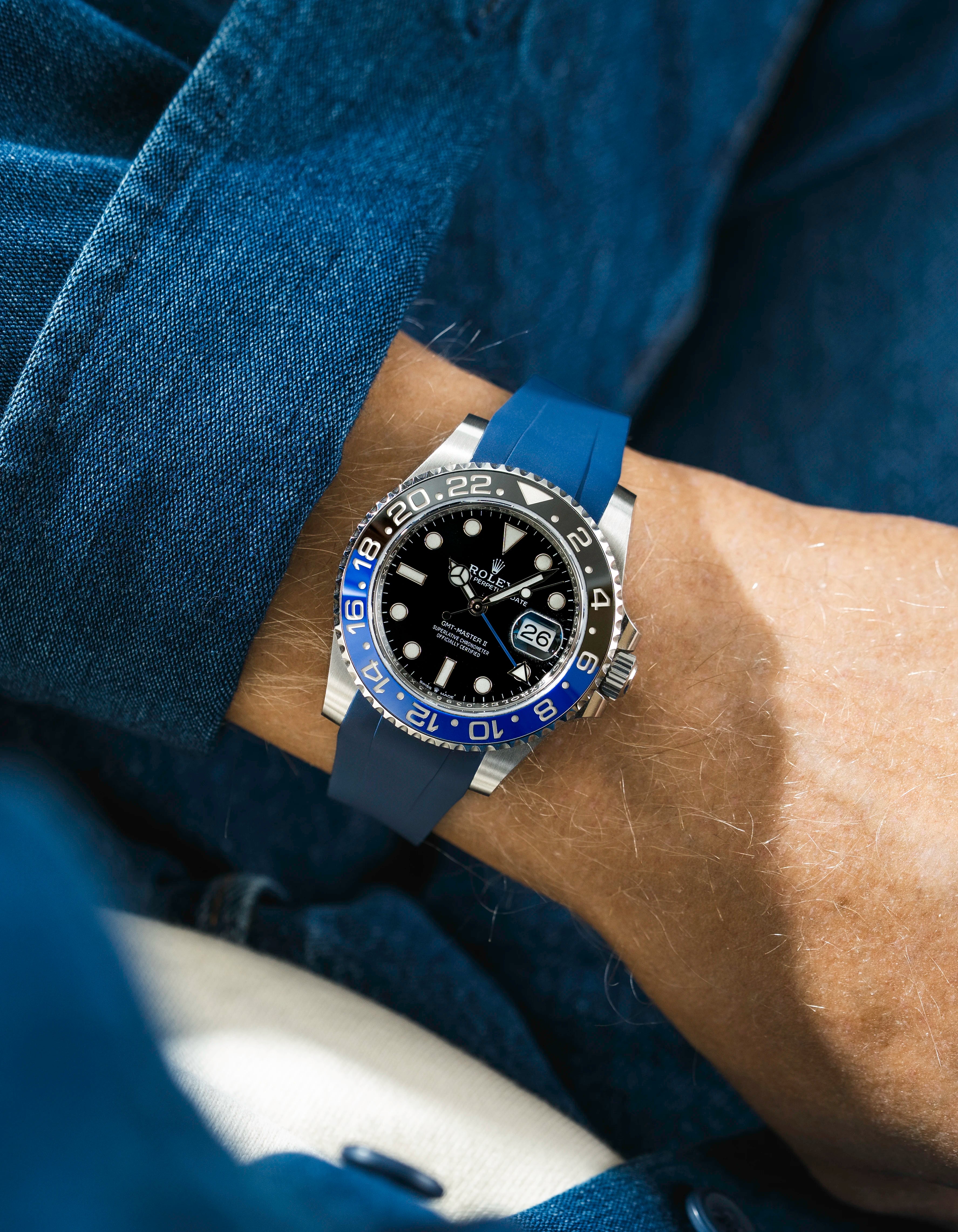 Close-up of a person wearing a Rolex GMT Master 2 Batman model watch with a blue jacket sleeve and a blue FKM rubber watch strap from Wristbuddys
