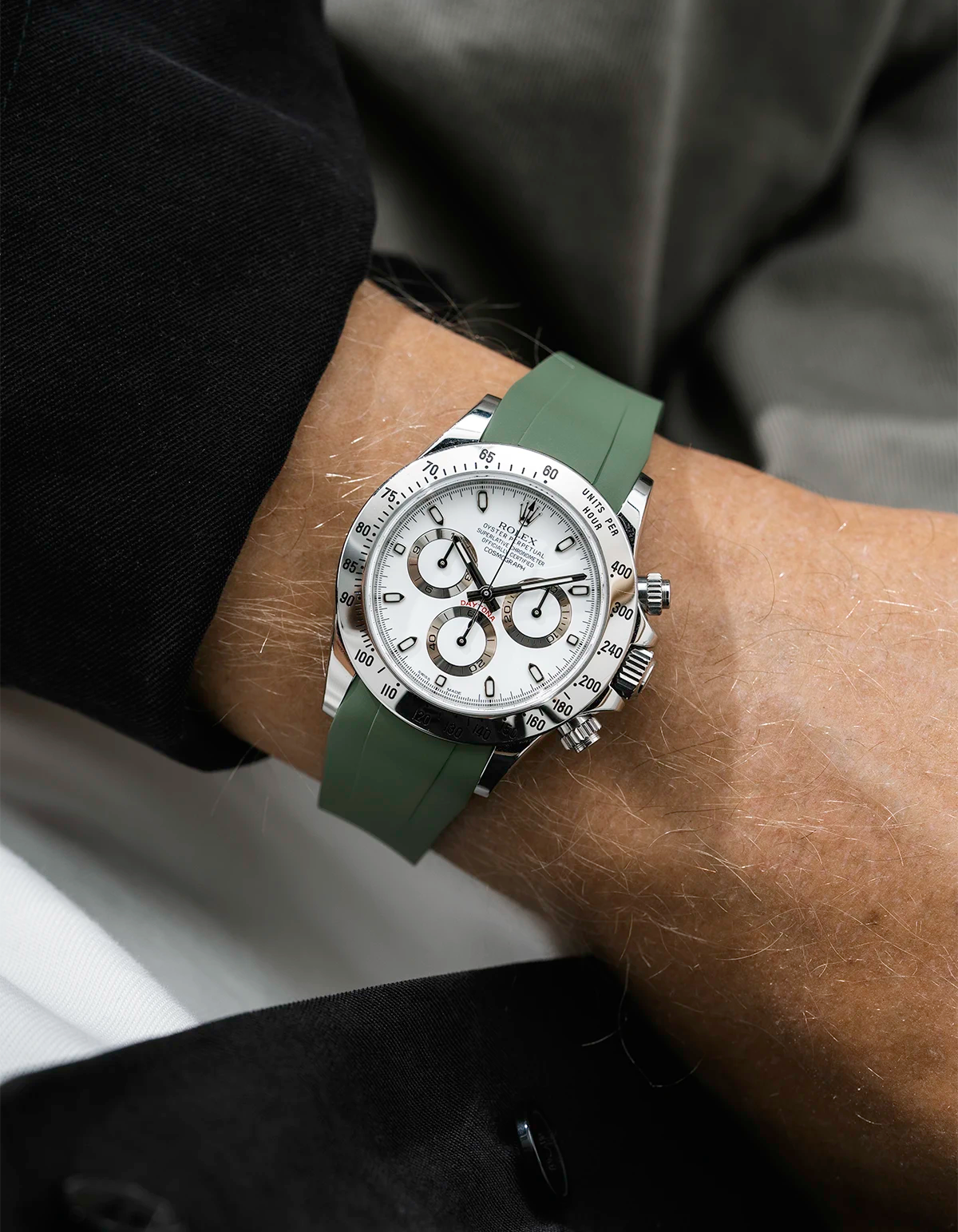 Close-up of a person wearing a white Rolex Daytona watch with a black jacket sleeve and a green FKM rubber watch strap from Wristbuddys
