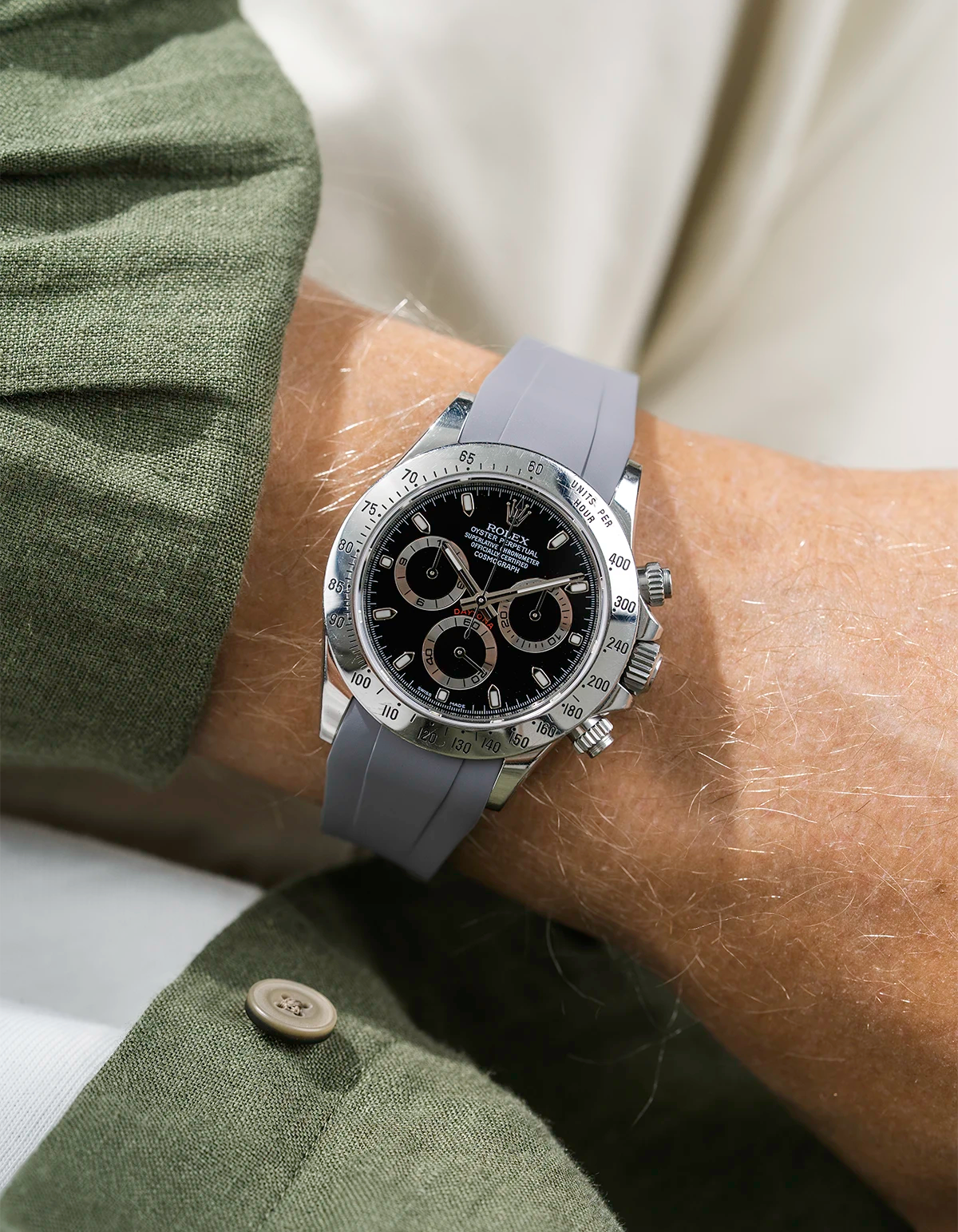 Close-up of a person wearing a black Rolex Daytona watch with a green jacket sleeve and a grey FKM rubber watch strap from Wristbuddys