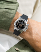 Close-up of a person wearing a black Rolex Daytona watch with a green stiped shirt sleeve and a black vertech FKM rubber watch strap from Wristbuddys
