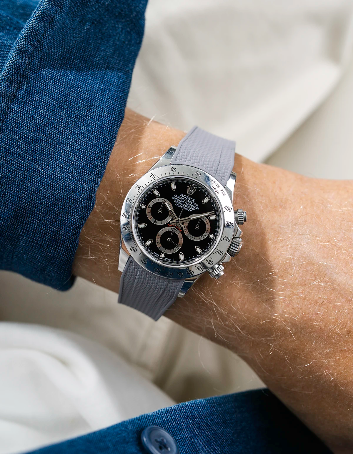 Close-up of a person wearing a black Rolex Daytona watch with a blue stiped shirt sleeve and a grey vertech FKM rubber watch strap from Wristbuddys