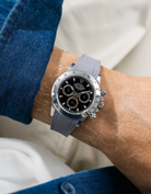 Close-up of a person wearing a black Rolex Daytona watch with a blue stiped shirt sleeve and a grey vertech FKM rubber watch strap from Wristbuddys