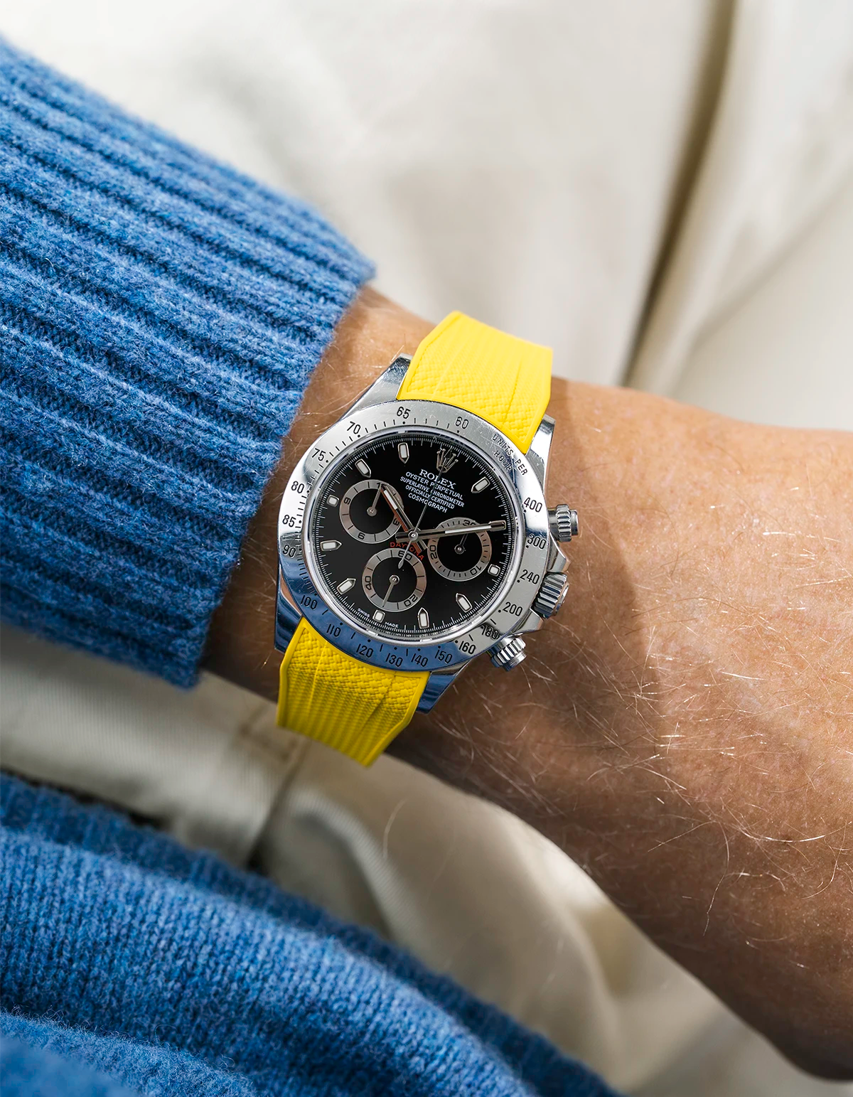Close-up of a person wearing a black Rolex Daytona watch with a blue wool sweatshirt and a yellow vertech FKM rubber watch strap from Wristbuddys