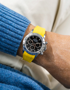 Close-up of a person wearing a black Rolex Daytona watch with a blue wool sweatshirt and a yellow vertech FKM rubber watch strap from Wristbuddys