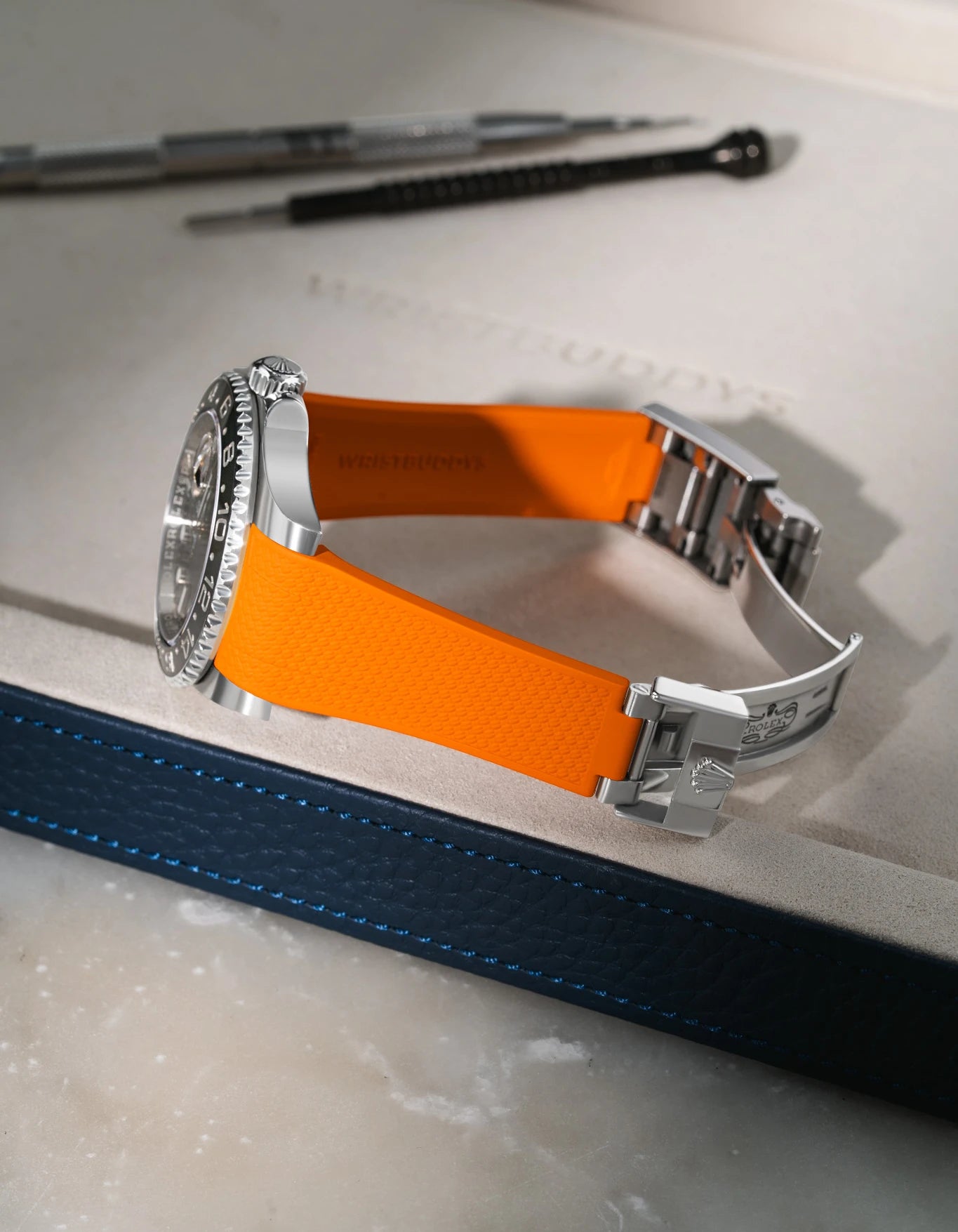 Orange textured FKM rubber watch band for Rolex GMT-Master II 116710, custom integrated fit for original clasp, resting on a grey valet tray.