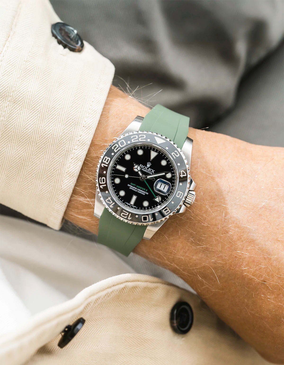 Close-up of a person wearing a Rolex GMT Master Green hand 116710 model watch with  beige jacket sleeve and a military green FKM rubber watch strap from Wristbuddys