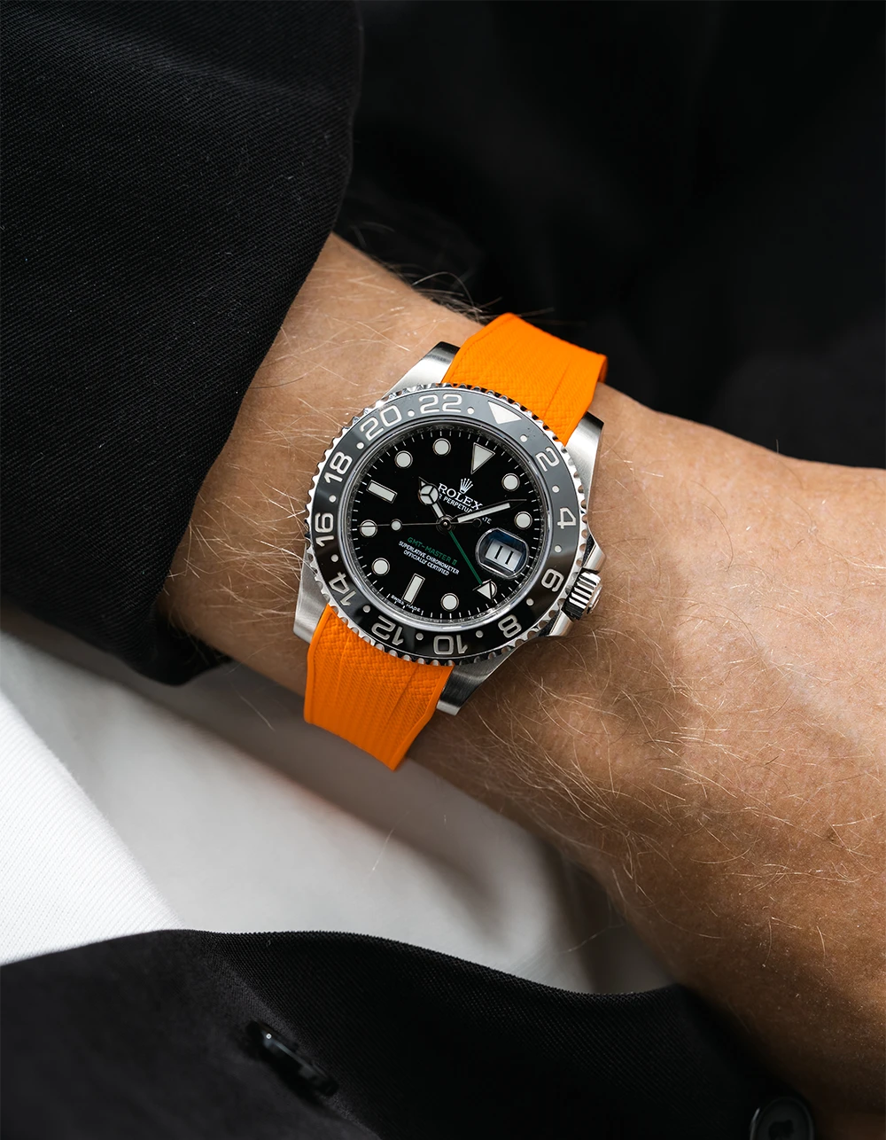Close-up of a person wearing a Rolex GMT Master Green hand 116710 model watch with black jacket sleeve and a orange vertech FKM rubber watch strap from Wristbuddys