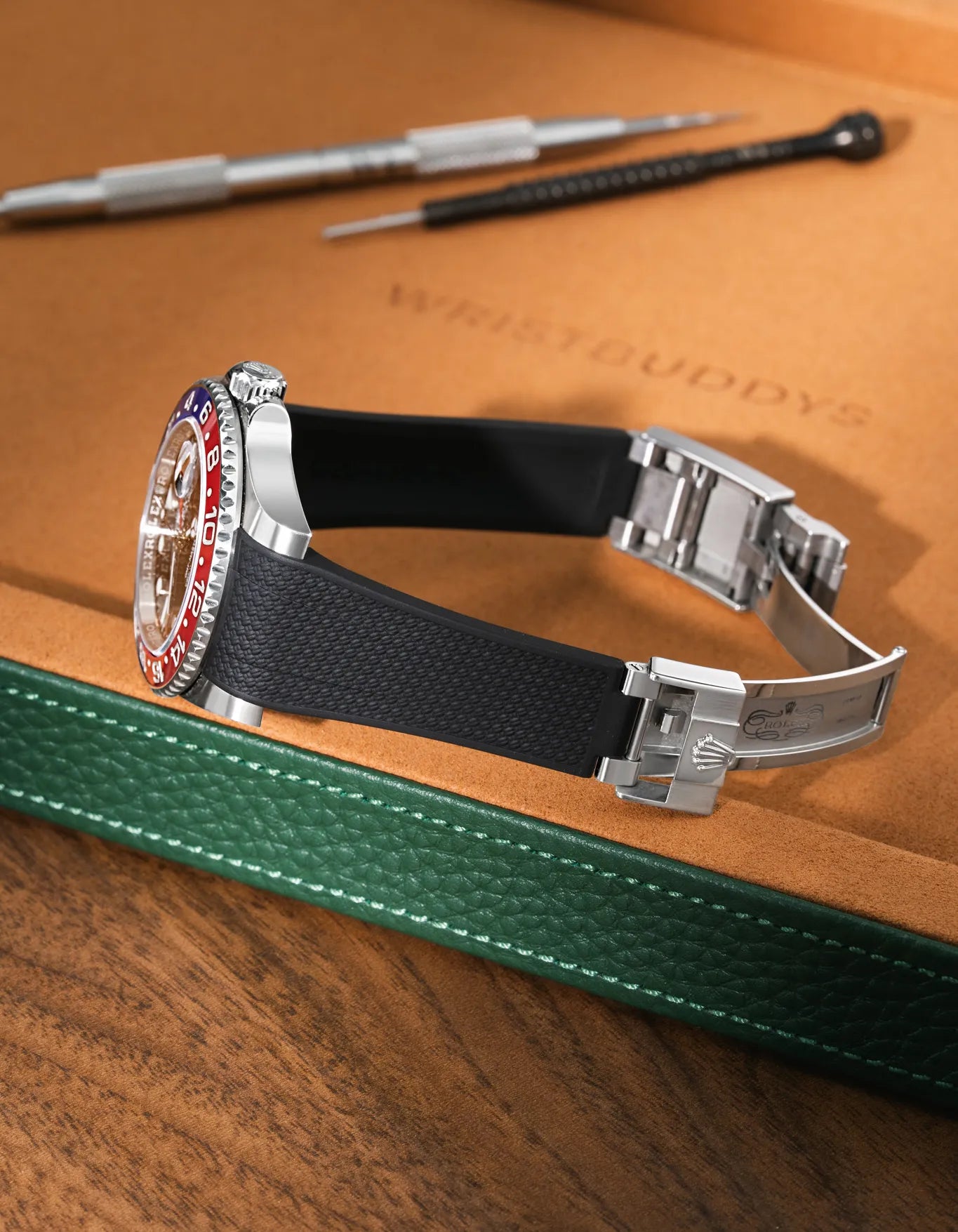 Black Vertech FKM rubber strap for Rolex GMT Master II 116710/126710, integrated seamless fit with original clasp, resting on a leather valet tray.