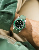 Close-up of a wrist wearing a Rolex Submariner on a Wristbuddys FKM Rubber watch strap & watch with a green face, against a blurred background.