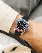 Close-up of a person wearing a Rolex GMT Master 2 Pepsi model watch with a beige jacket sleeve and a black FKM rubber watch strap from Wristbuddys