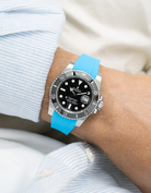 Wrist wearing a Rolex Submariner on a capri blue  Wristbuddys FKM Rubber watch strap and white shirt background