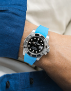 Rolex Submariner on a capri blue Wristbuddys FKM Rubber watch strap on a wrist, wearing a blue shirt.