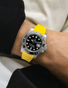 Rolex Submariner on a yellow vertech Wristbuddys FKM Rubber watch strapon a wrist against a neutral background