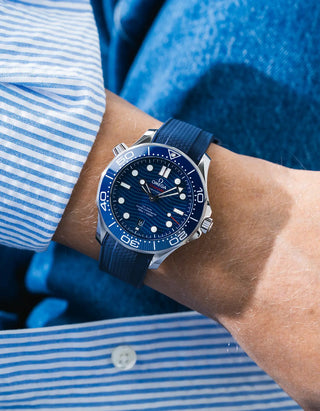Blue Vertech rubber strap for Omega Seamaster Diver 300 42mm – worn on wrist with light blue striped shirt, blue dial and bezel, blue jacket background, front angle view