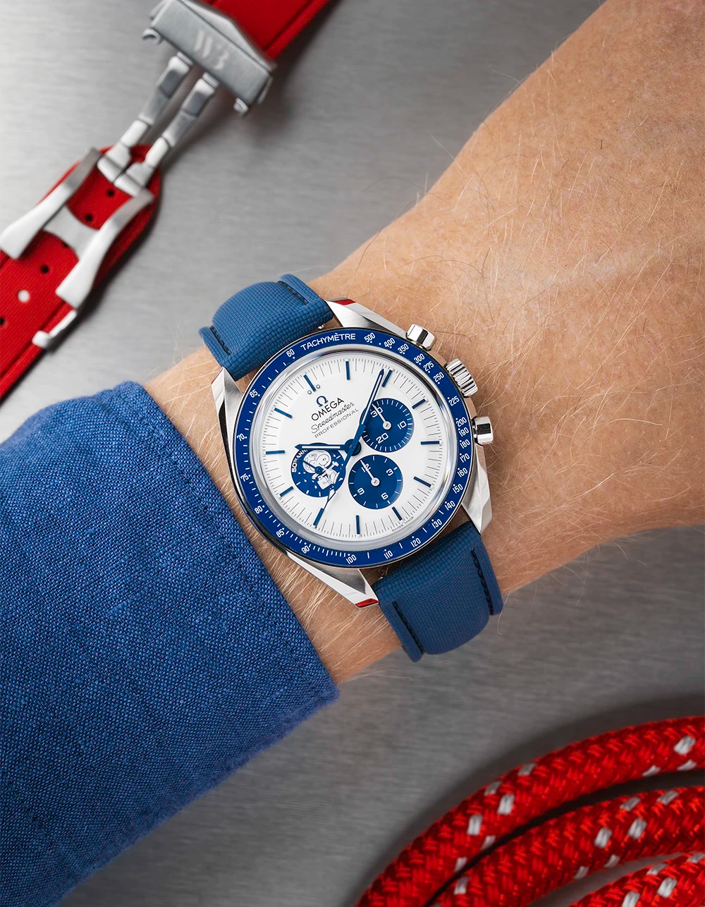 Wrist wearing a blue Omega Speedmaster with a detailed face on a wrist with a blue sleeve.