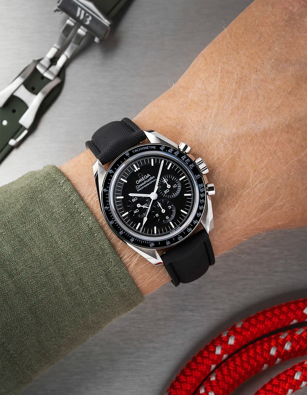 Black Omega Speedmaster with a detailed face on a person's wrist, with a blurred background