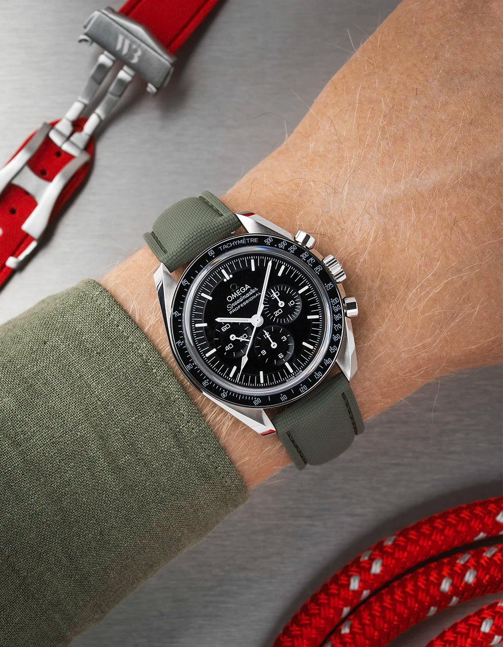 Wrist wearing a black Omega Speedmaster  with a detailed face on a wrist with a green sleeve.