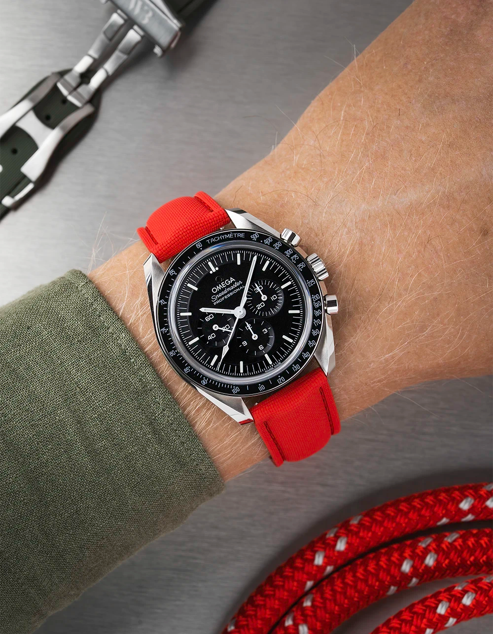 Omega Speedmaster with a black face and red strap on a wrist, with additional straps in the background.