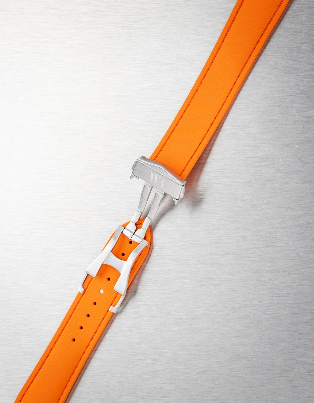 Orange watch strap with silver clasp on a textured gray background
