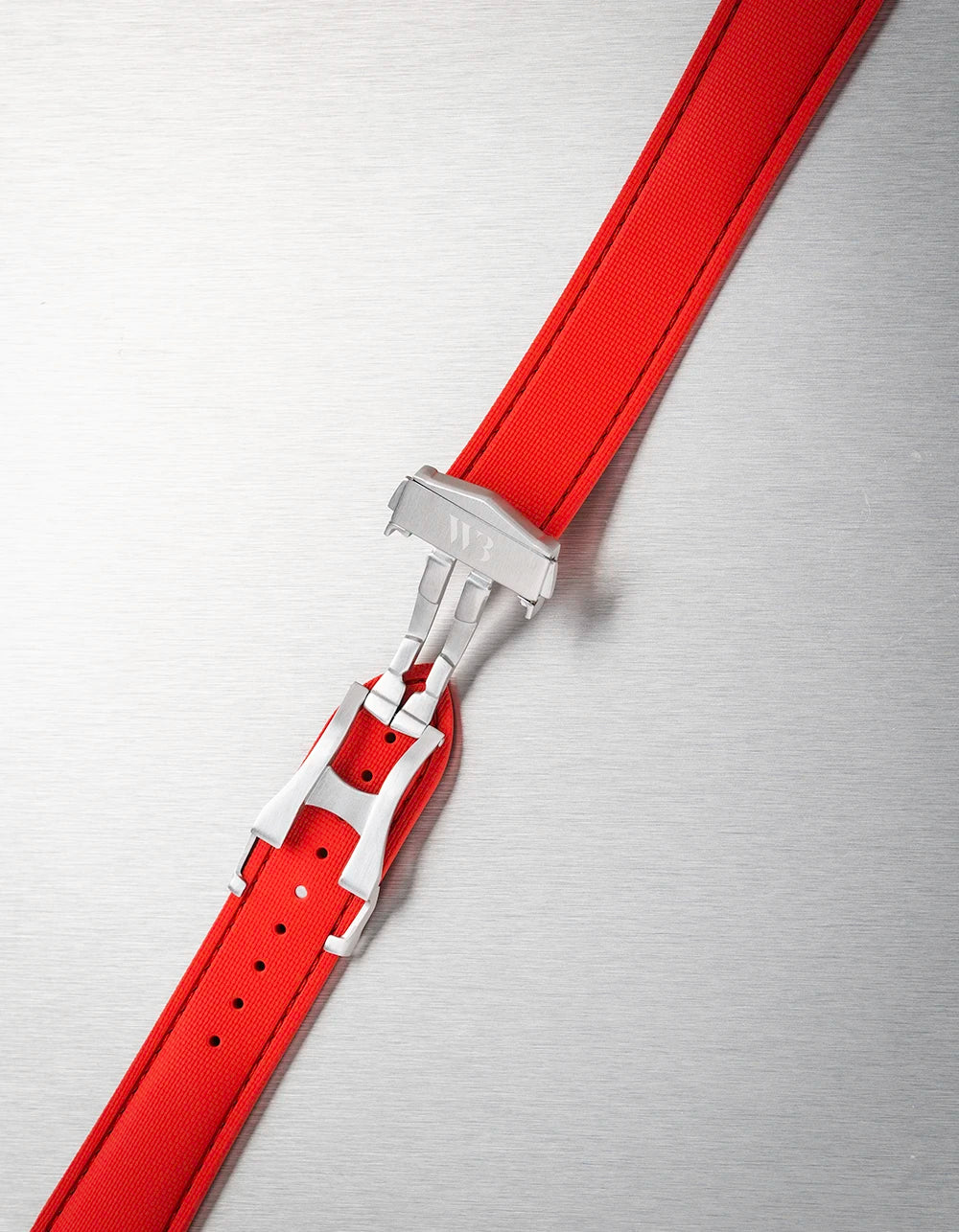 Red rubber watch strap with silver buckle on a metallic surface