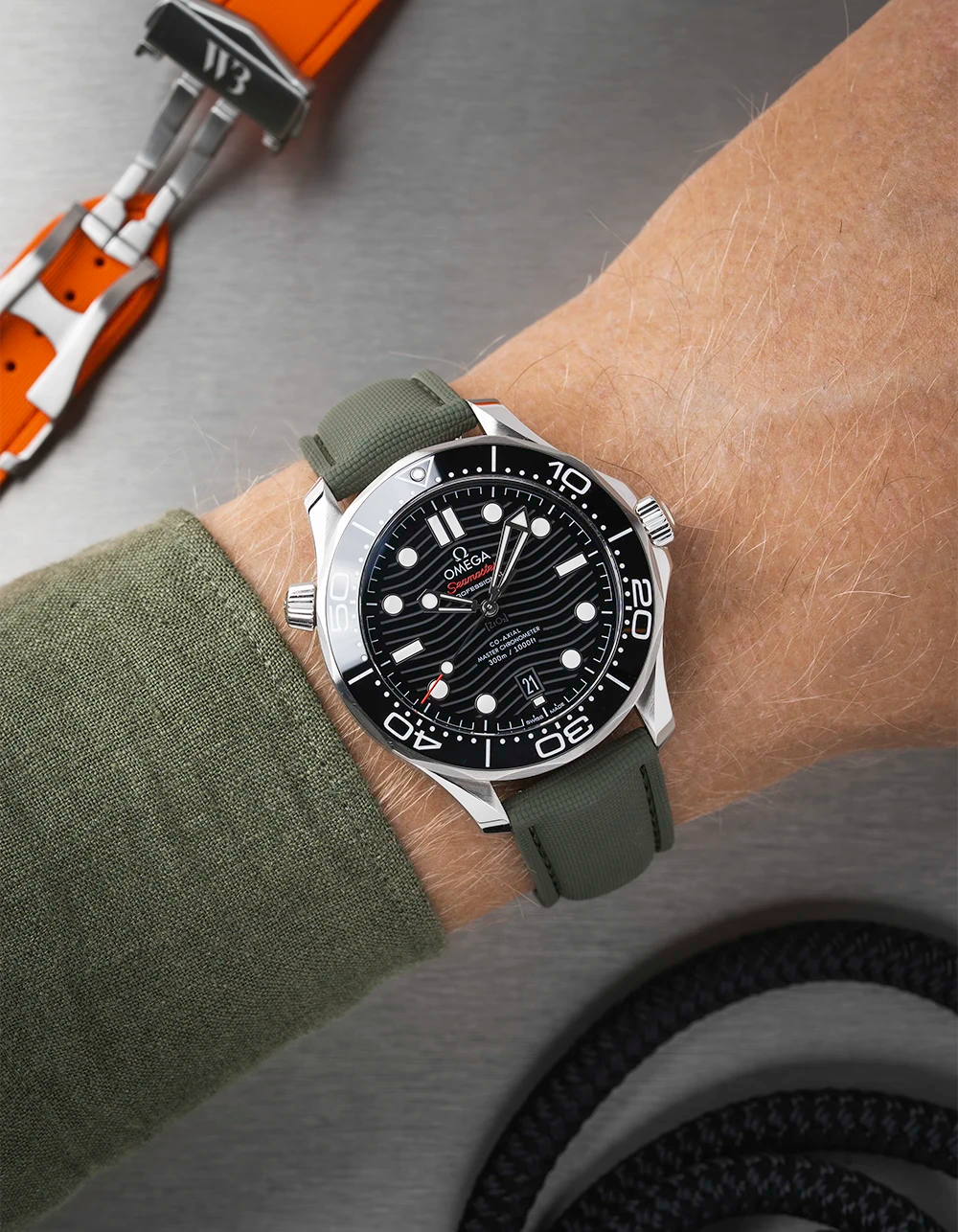 Wrist wearing a black Omega Seamaster  with a detailed face on a wrist with a green sleeve.