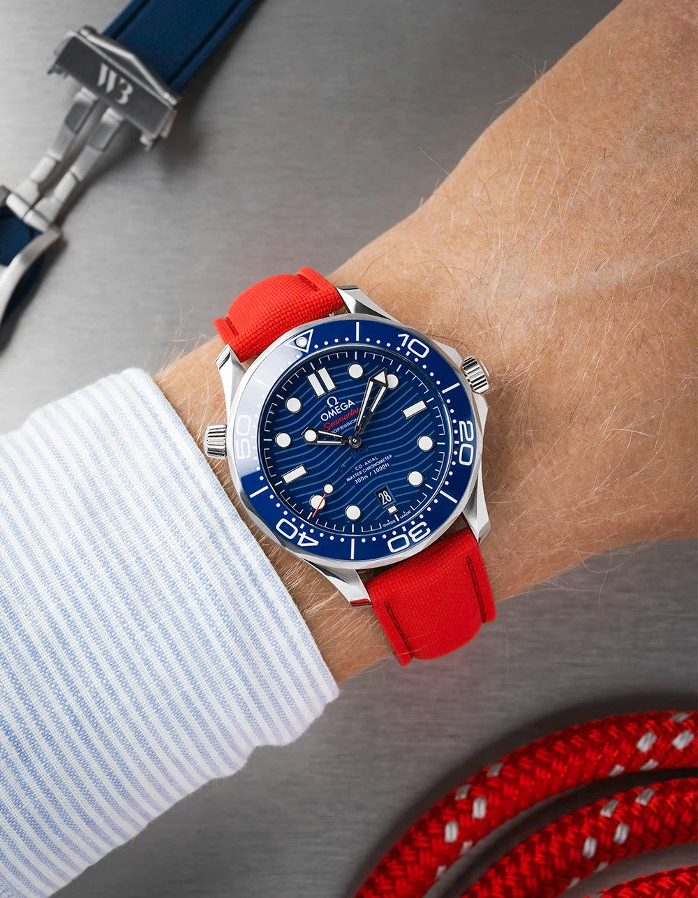 Omega Seamaster with a blue face and red strap on a wrist, with additional straps in the background.