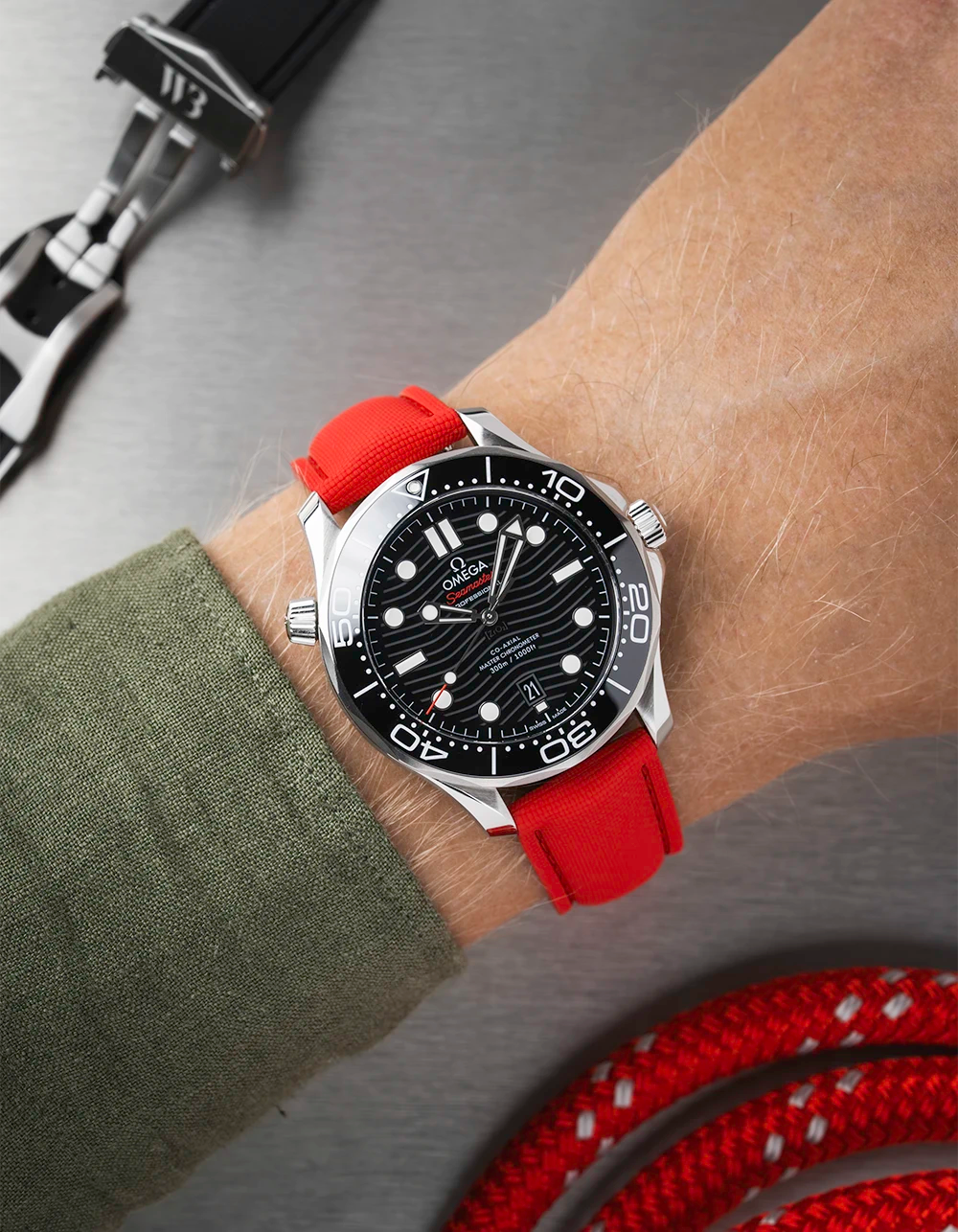 Omega Seamaster with a black face and red strap on a wrist, with additional straps in the background.