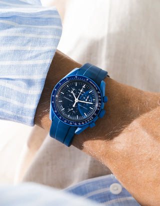 Smooth blue rubber strap fitted to an OMEGA x Swatch MoonSwatch Mission to Neptune watch, worn on the wrist in a lifestyle shot with clothing visible