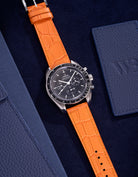 Omega Speedmaster watch with bright orange alligator leather strap on a dark blue background